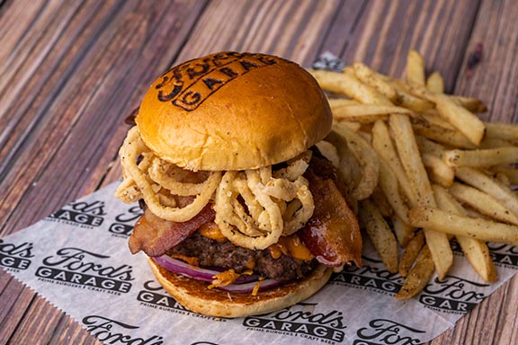 Image of a burger with fried onion strings and bacon slices on it, from Ford's Garage.