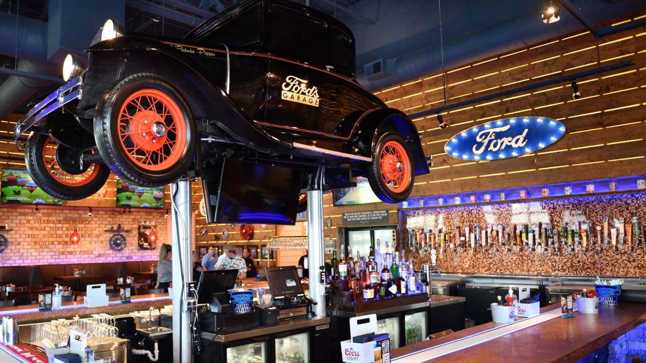 Interior of Ford's Garage, there is a vintage Ford vehicle lifted on metal supports above the bar area.